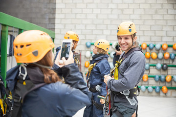 Woman with smart phone photographing man preparing zip line equipment