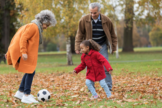 Grandparents playing soccer with granddaughter in autumn park