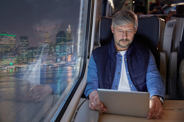 Man using digital tablet on passenger train at night