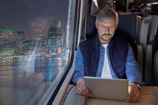 Man Using Digital Tablet On Passenger Train At Night