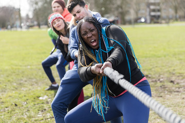 Determined team pulling rope in tug-of-war at park