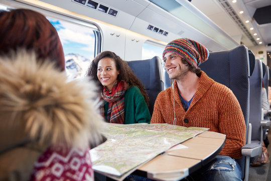 Smiling young friends planning with map on passenger train
