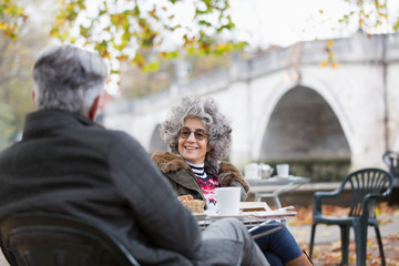 Active senior couple talking, enjoying coffee at autumn park cafe