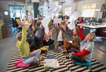 Playful, enthusiastic creative business team throwing paperwork overhead in open plan office