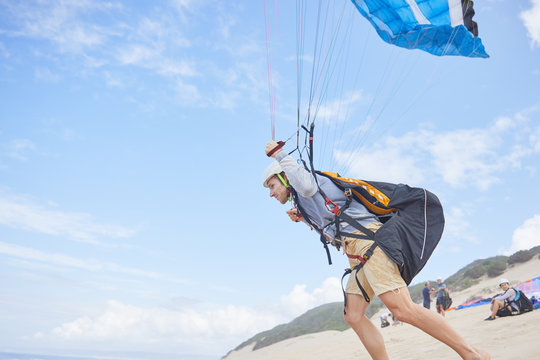 Male paraglider running with parachute on beach