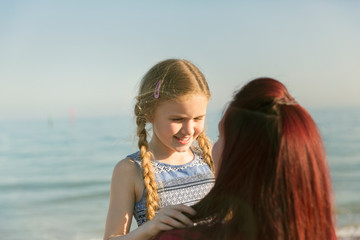 Affectionate mother holding daughter on sunny ocean beach