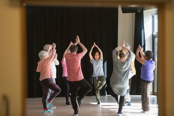 Active seniors exercising in circle, practicing yoga tree pose