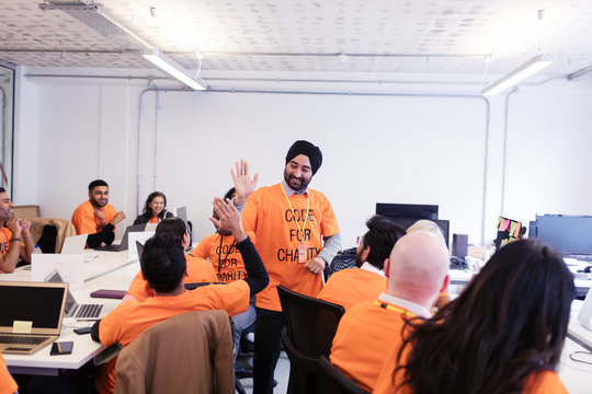 Hackers celebrating, high-fiving and coding for charity at hackathon