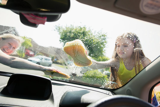 Mother and daughter washing car windshield