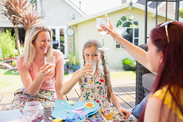 Lesbian couple and daughter drinking on sunny patio
