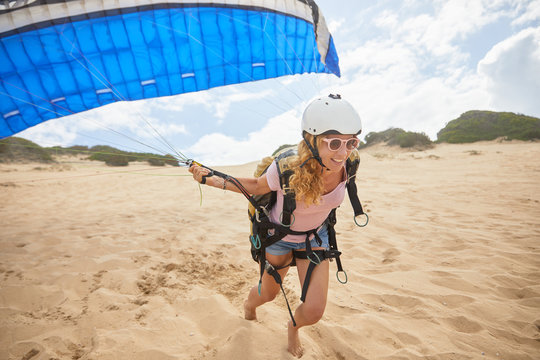 Smiling female paraglider running with parachute on beach