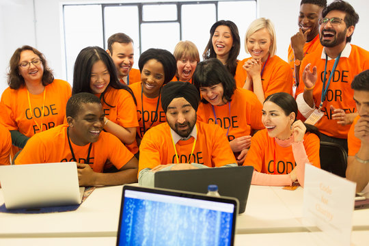 Happy hackers sharing laptop, coding for charity at hackathon