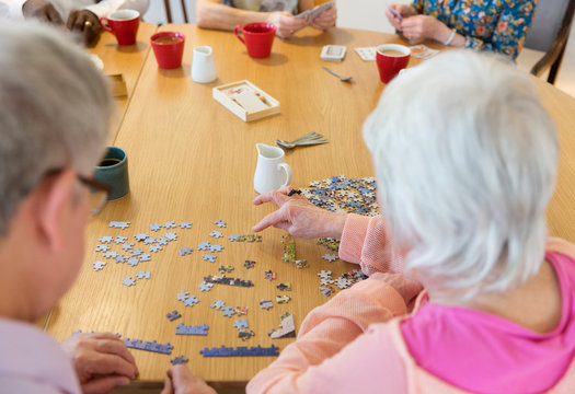Senior friends assembling jigsaw puzzle at table in community center