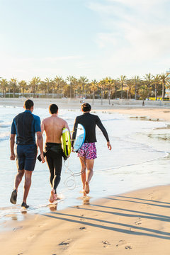 Male surfers walking with surfboards on sunny ocean beach