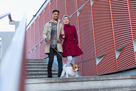 Smiling young couple walking dog down urban, modern stairs