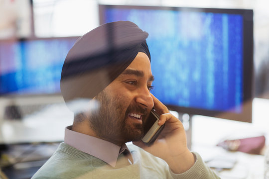 Indian computer programmer in turban talking on smart phone in office