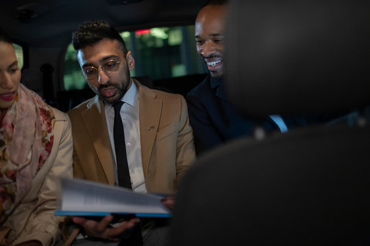 Business people discussing paperwork in back seat of crowdsourced taxi