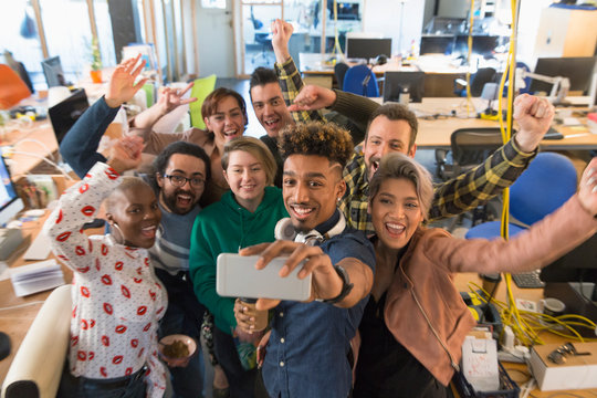 Enthusiastic creative business team cheering, taking selfie in office