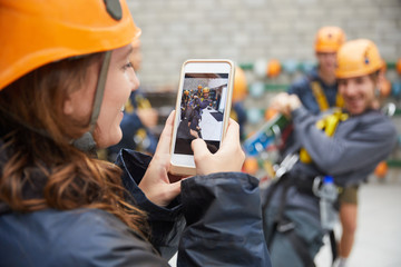 Woman with camera phone photographing friends in zip line equipment