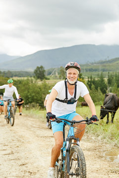 Smiling, confident mature man mountain biking on rural dirt road