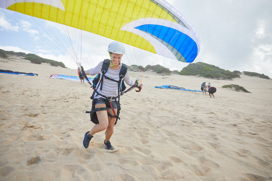 Female paraglider with parachute running, taking off on beach