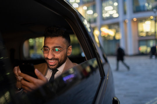 Businessman using smart phone in crowdsourced taxi at night