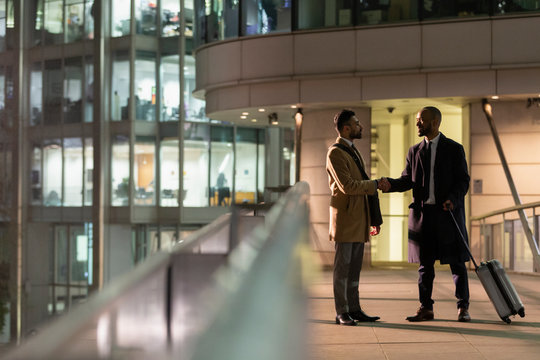Businessmen suitcase handshaking on urban pedestrian bridge at night - Powered by Adobe