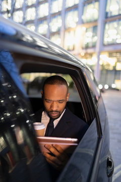 Businessman drinking coffee, using digital tablet in crowdsourced taxi