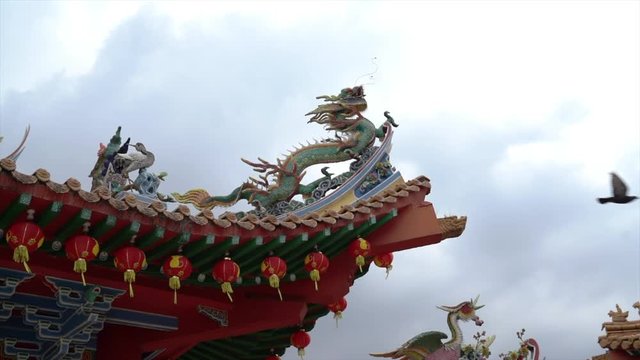 Temple roof with beautiful carvings, paintings and hanging red lanterns. And a bird fly across the scene. Slow motion.