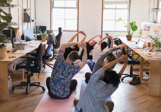 Creative business people stretching, practicing yoga in office