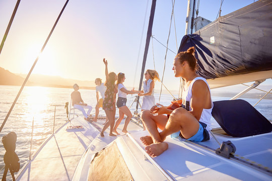 Playful friends dancing, playing guitar on sunny catamaran