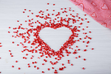 Heart shaped from pomegranate seeds on white table.