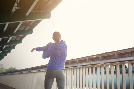 Young female runner stretching arms along urban railing