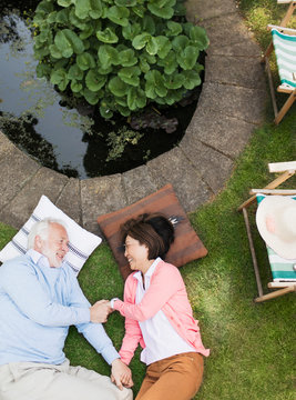 Affectionate senior couple laying by pond in garden