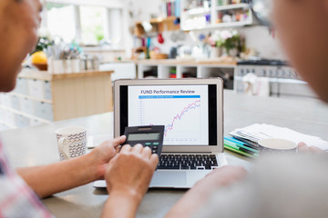 Senior man with calculator looking at investment chart on laptop