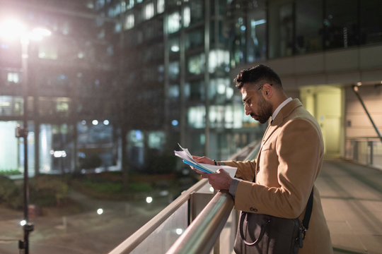 Businessman reviewing paperwork on urban pedestrian bridge at night