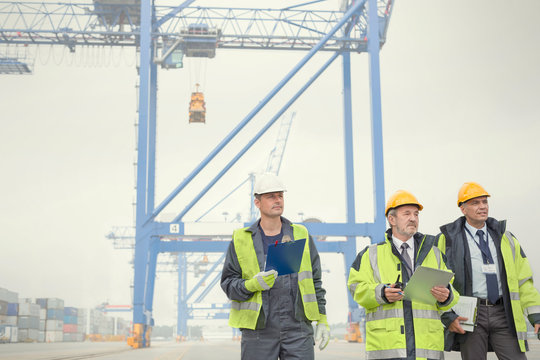 Dock workers and manager walking below crane at shipyard