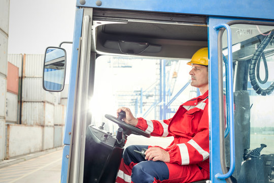 Dock worker operating cargo container forklift at shipyard