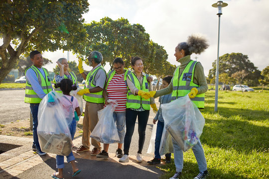 Happy volunteers celebrating, cleaning litter from sunny park - Powered by Adobe