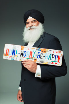 Portrait smiling, well-dressed senior man in turban holding  Dont Worry Be Happy  license plates