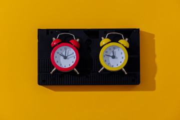 Two vintage alarm clocks and VHS cassette on yellow background