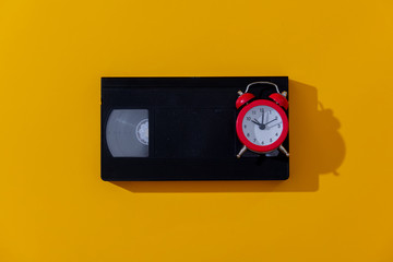 Red alarm clock and VHS cassette on yellow background