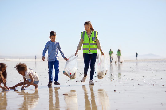 Mother and son volunteers cleaning up litter on sunny wet sand beach