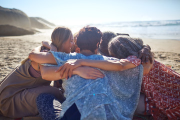 Group hugging in circle on sunny beach during yoga retreat