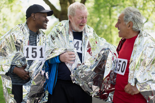 Active senior men friends finishing sports race, wrapped in thermal blankets