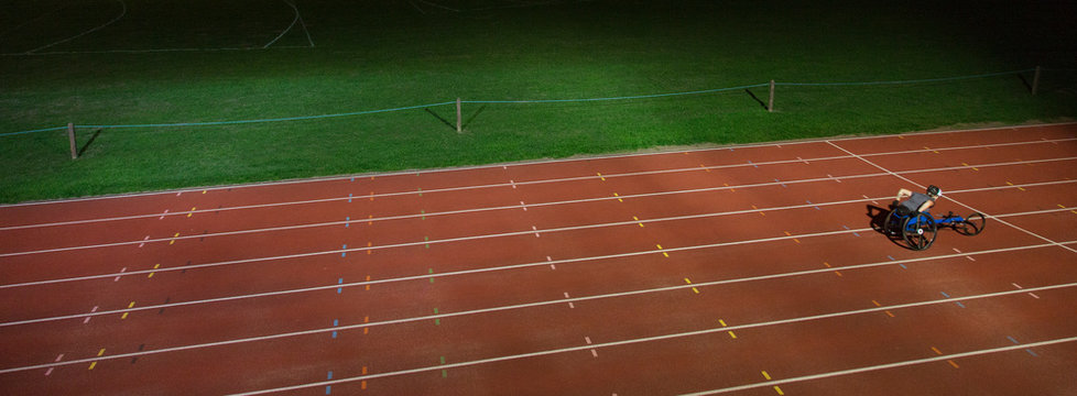 Paraplegic athlete training for wheelchair race on sports track at night