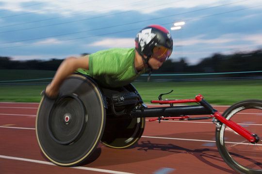 Determined young male paraplegic athlete speeding along sports track in wheelchair race