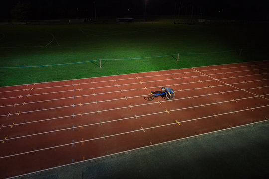 Paraplegic athlete speeding along sports track in wheelchair race at night