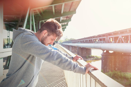Male runner stretching, leaning against sunny urban railing