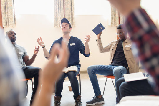 Men with bible praying with arms raised in prayer group